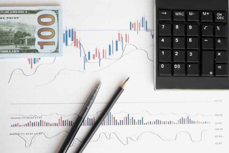 Mesa de trabalho com gráficos financeiros, calculadora e cédulas, representando análise econômica.